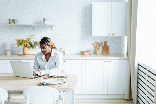 Woman Typing on a Laptop While in the Kitchen